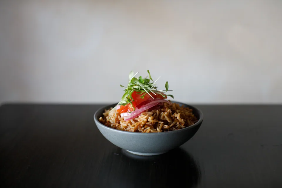 Swahili pilau topped with kachumbari in a ceramic bowl