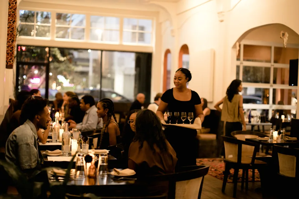 A server carrying a tray of wine glasses through the candlelit dining room