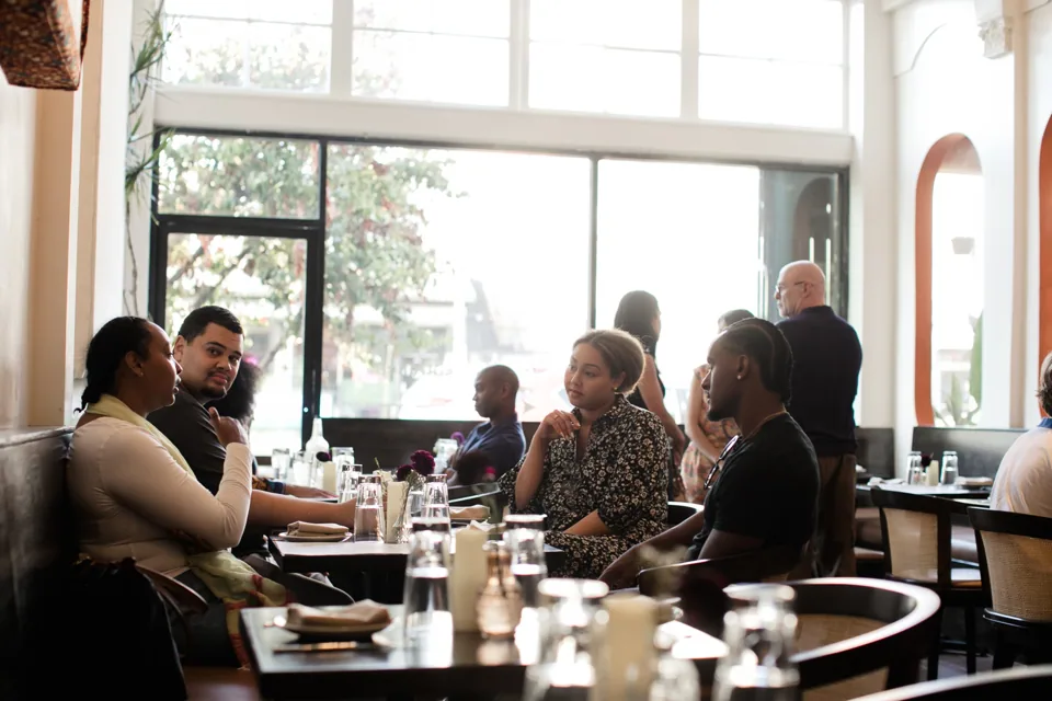 Guests talking around tables beside the dining room’s tall windows